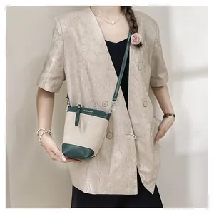 Détail du sac seau en toile avec bordure en cuir vert et logo MYCARE porté par un mannequin