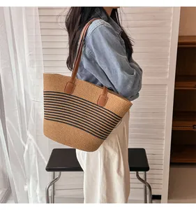 Detail of straw tote bag with black horizontal stripes and brown leather handles