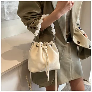 Detail of cream drawstring bucket bag featuring a decorative pearl handle on a female model