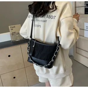 Detail van hobo-emmer tas met zilveren ketting, kwastje en riem op een model