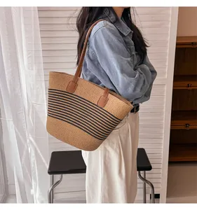 Detail of woven straw tote bag with black stripes and brown faux leather shoulder straps
