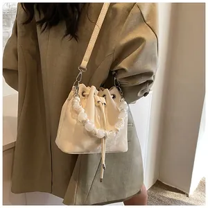 Close-up of beige drawstring bucket bag with clear beaded handle and crossbody strap