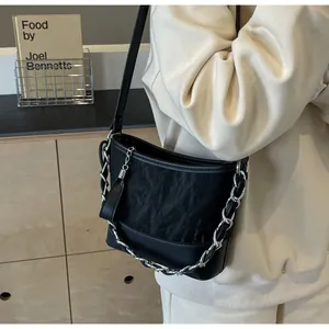Detail van zwarte bucket bag met textuur, zilveren ketting en lederen kwastjes