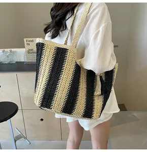Dettaglio di una grande borsa tote in paglia a righe verticali nere e beige con nappe