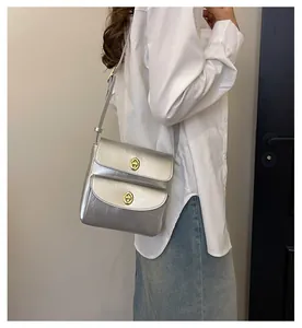 Detail van zilveren crossbodytas van gekreukt leer met gouden draaisluitingen op een model