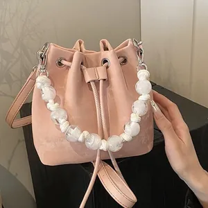 Pink drawstring bucket bag with decorative pearl handle and adjustable shoulder strap