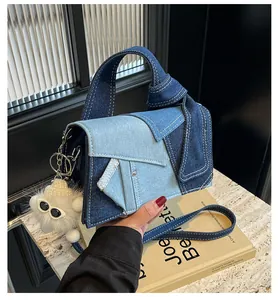 Detail of denim patchwork tote with white stitching and plush doll charm accessory