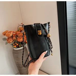 Détail d'un sac seau en cuir noir avec bandoulière chaîne et fermoir boule dorée