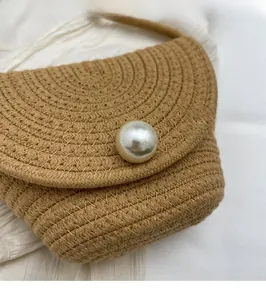 Detailed close-up of handmade woven straw bag featuring a large pearl embellishment