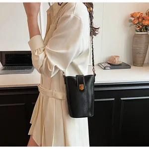 Détail du sac seau en cuir noir avec fermoir doré et bandoulière chaîne sur un bureau
