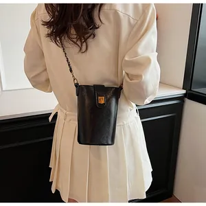 Détail d'un mini sac seau en cuir noir avec bandoulière chaîne dorée et fermoir métal