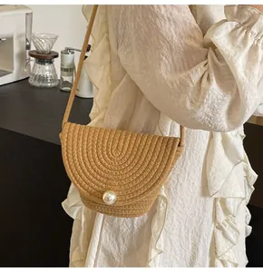 Detail of hand-woven semi-circle straw bag featuring a large pearl clasp and woven strap