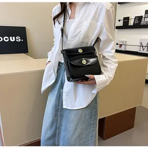 Detail van een zwarte crossbodytas met geplooide textuur en dubbele gouden draaisluitingen