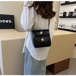 Model draagt een zwarte minimalistische crossbodytas met dubbele gouden draaisluitingen