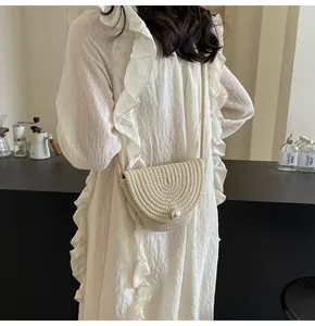 Detail of hand-woven beige bucket bag with elegant pearl clasp on a white ruffle dress