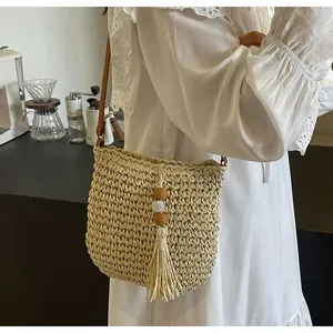Detail van handgeweven beige strooien emmertas met bruine riem en decoratieve kwast
