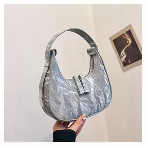 Detail van een zilveren metallic halve maan tas met plissé textuur en dubbele ritsen