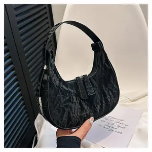 Detail van de zwarte geplooide textuur op de halvemaanvormige tas met zilveren hardware