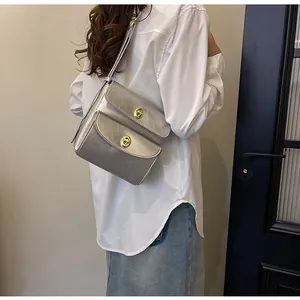 Zilveren metallic schoudertas met gouden draaisluitingen gedragen door een model in stijl