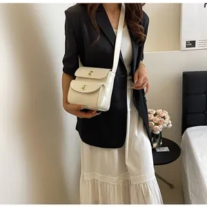 Detail van een crèmekleurige crossbodytas met dubbele gouden gespen op een vrouwelijk model