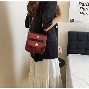 Detailopname van een vintage bordeauxrode leren crossbody tas met gouden draaisluitingen