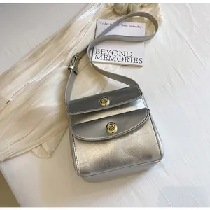 Detail van zilveren crossbodytas met gebarsten textuur en dubbele gouden draaisluitingen