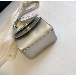 Detailopname van zilveren crossbodytas met textuur en dubbele metalen draaisluitingen
