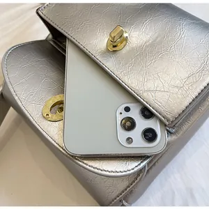 Detail van zilveren geplooide crossbodytas met gouden slot en ruimte voor smartphone