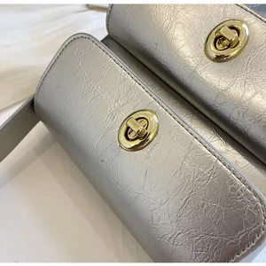 Detail van de zilveren crossbodytas van kreukelleer met gouden draaisluitingen