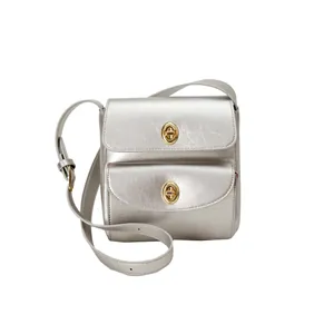Detail van zilveren metallic crossbodytas met dubbele gouden draaisluitingen