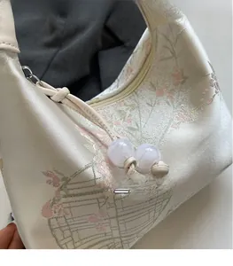 Close-up of floral embroidery on ivory brocade bag with beaded zipper pulls