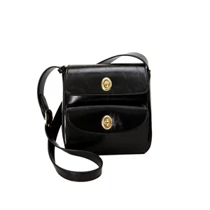 Detailopname van zwarte crossbodytas met glanzende lakleertextuur en gouden metalen sluitingen