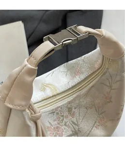 Close-up of shiny silver metal buckle and exquisite floral embroidery on beige handbag