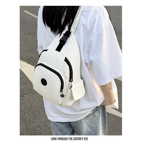 Detail view of white nylon chest bag with black contrast zippers and logo in outdoor setting