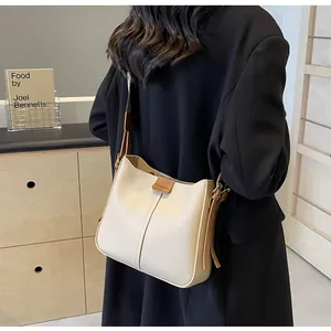 Detail van een crèmekleurige schoudertas met bruine riem op een zwarte blazer