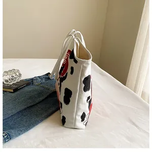 Close-up of canvas tote bag with cow print and artistic pattern on white bedding