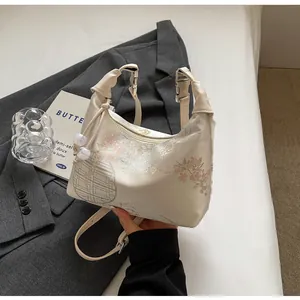 Detail view of the embroidered floral dumpling bag with satin finish and pearl charm