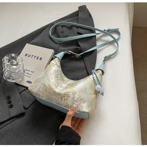 Detail of light blue jacquard half-moon bag with pearl pendant on a grey blazer