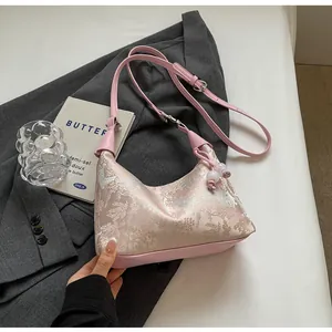 Detailed close-up of pink embroidered dumpling bag with classic Chinese pattern and bead tassel