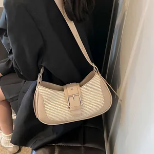 Detail of a khaki underarm baguette bag with woven straw panel and metal buckle strap