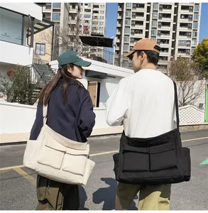 Detail of canvas messenger bags in black and beige with dual flap pockets and wide straps