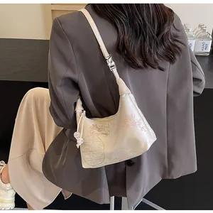 Detail of cream crossbody bag with floral embroidery and elegant bead charm strap