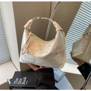 Close-up of beige embroidered hobo bag with pink floral patterns and beaded charms