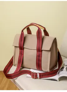 Detail of khaki canvas tote bag with red striped handles and metal buckle on magazine