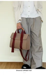 Detail of canvas tote bag with red striped handles and long strap on model shoulder
