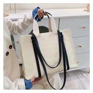 Sac cabas en toile avec lanières en cuir noir et coutures sur un meuble blanc