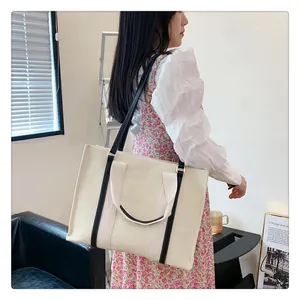 Détail d'un grand sac cabas en toile beige avec bandoulières noires porté par un mannequin