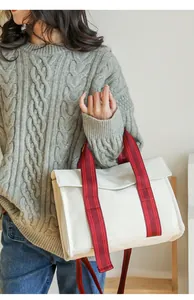 Detail of a beige canvas tote bag with red striped handles worn by a model in casual style