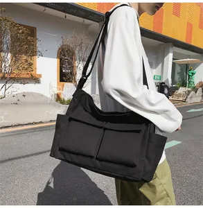Detail of a black canvas messenger bag featuring large front pockets and wide strap