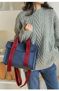 Detail of navy canvas tote bag with red-brown striped handles and crossbody strap